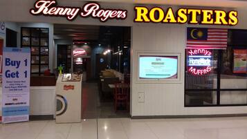 Un restaurant Kenny Rogers Roasters avec une enseigne au néon, une affiche d’offre d’emploi et une promotion du type « achetez-en un, obtenez-en un gratuitement ».
