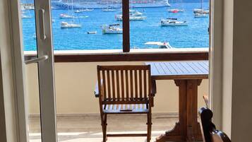 A balcony with a wooden bench and table, overlooking a marina with boats and a cruise ship.