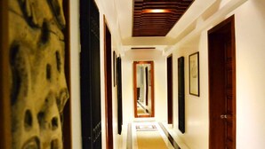Un couloir avec un mur orné de motifs, des portes en bois et des tableaux encadrés accrochés aux murs.
