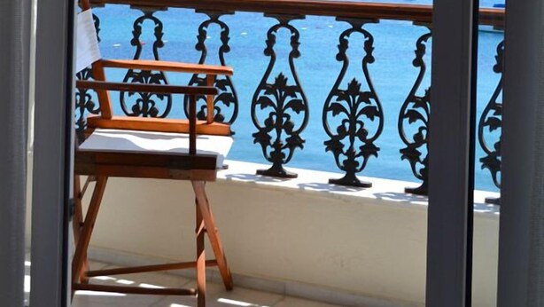 Un balcon avec une chaise en bois et une vue sur un port où sont amarrés des bateaux, avec une colline en arrière-plan.