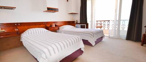 A hotel room with two beds, a balcony with a view, and a wooden headboard.