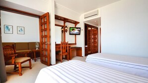 Une chambre d’hôtel avec deux lits, un bureau en bois, une chaise, un téléviseur et un climatiseur fixé au mur.