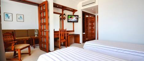 A hotel room with two beds, a wooden desk, a chair, a television, and a wall-mounted air conditioning unit.