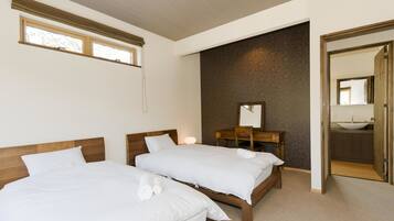 A hotel room with two beds, a wooden headboard, a brick accent wall, a wooden dresser, and a bathroom visible through an open door.