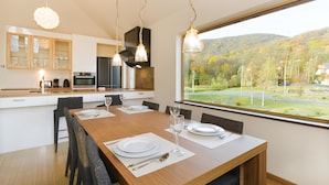 A modern kitchen with a dining area, large windows, and a view of a green landscape. - Hana & Jo (Kutchan)