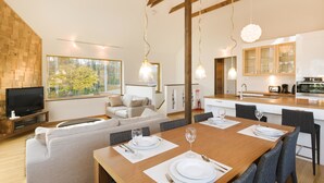 A modern living room with a sofa, dining table set for two, and a kitchen in the background. - Hana & Jo (Kutchan)