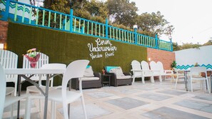 Un área de estar al aire libre con sillas y mesas de plástico blanco, una pared verde con el texto "Pavon Underwater Garden Resort" y una barandilla azul.