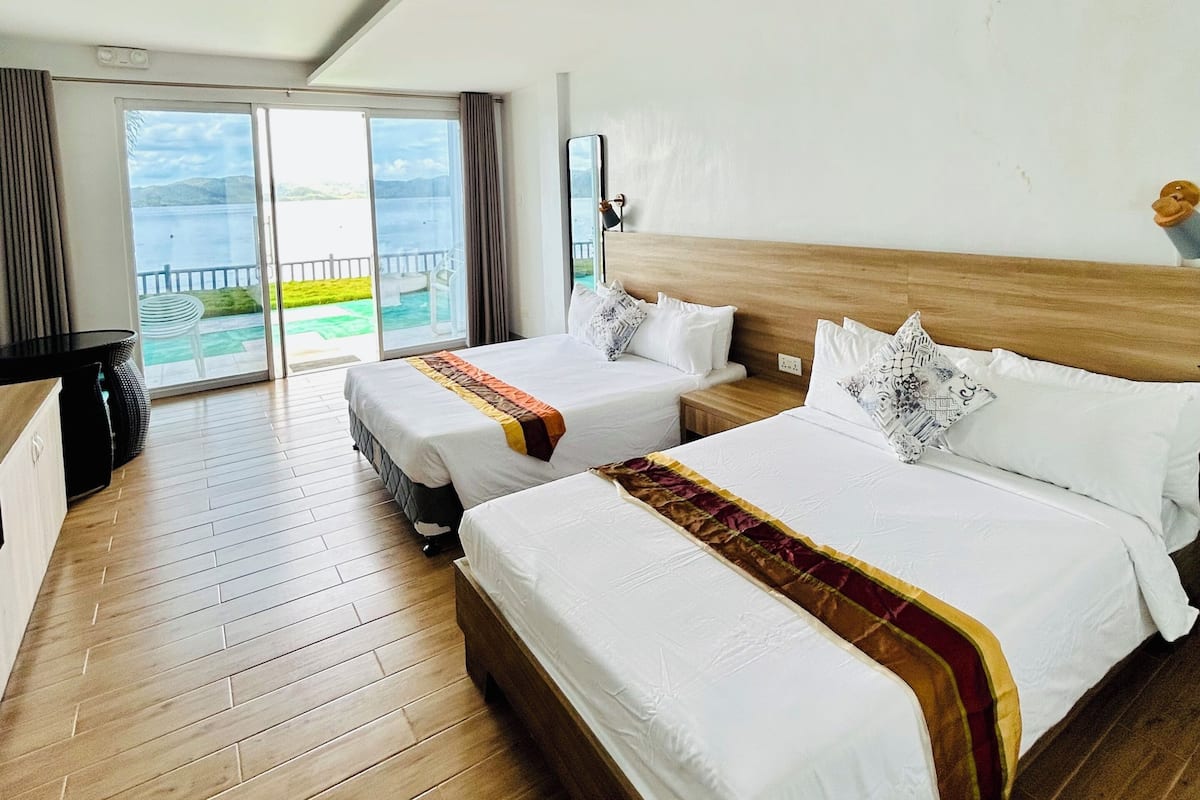 A hotel room with two beds, a large window with a view, and a wooden floor.