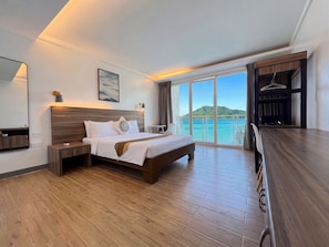 A hotel room with a bed, bedside table, a desk, a chair, a large window with a view of the sea, and a wardrobe. - Coron Underwater Garden Resort (Coron)