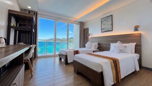 Habitación de hotel con dos camas, un escritorio y vista al mar.