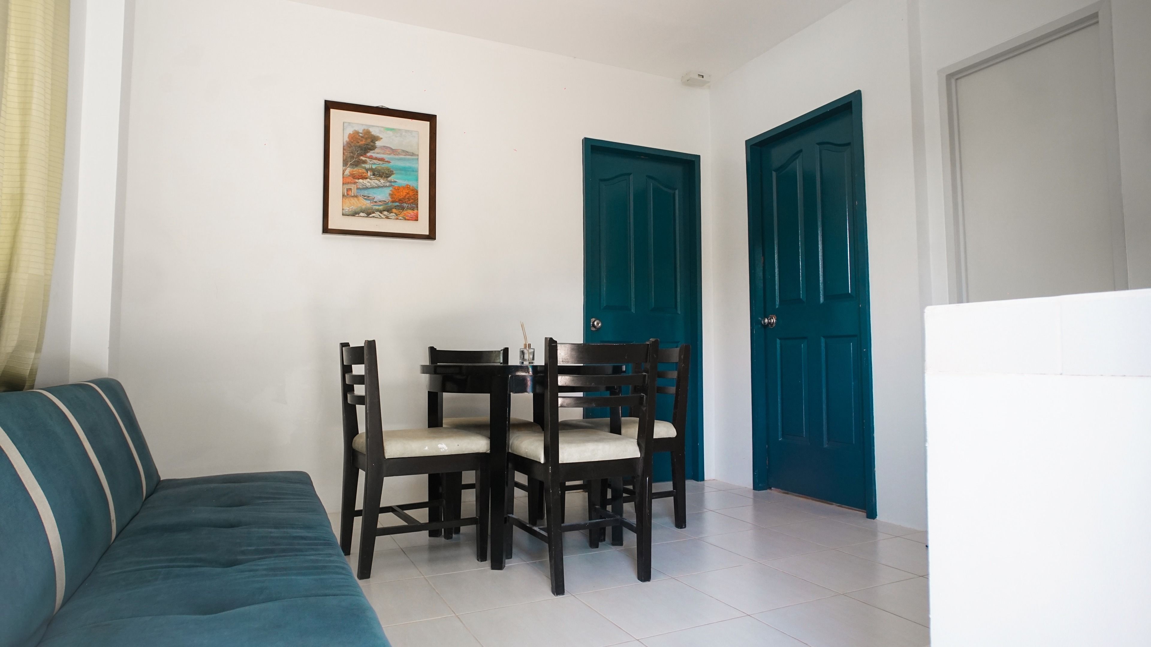 A room with a teal sofa, a dining table with four chairs, and two blue doors.