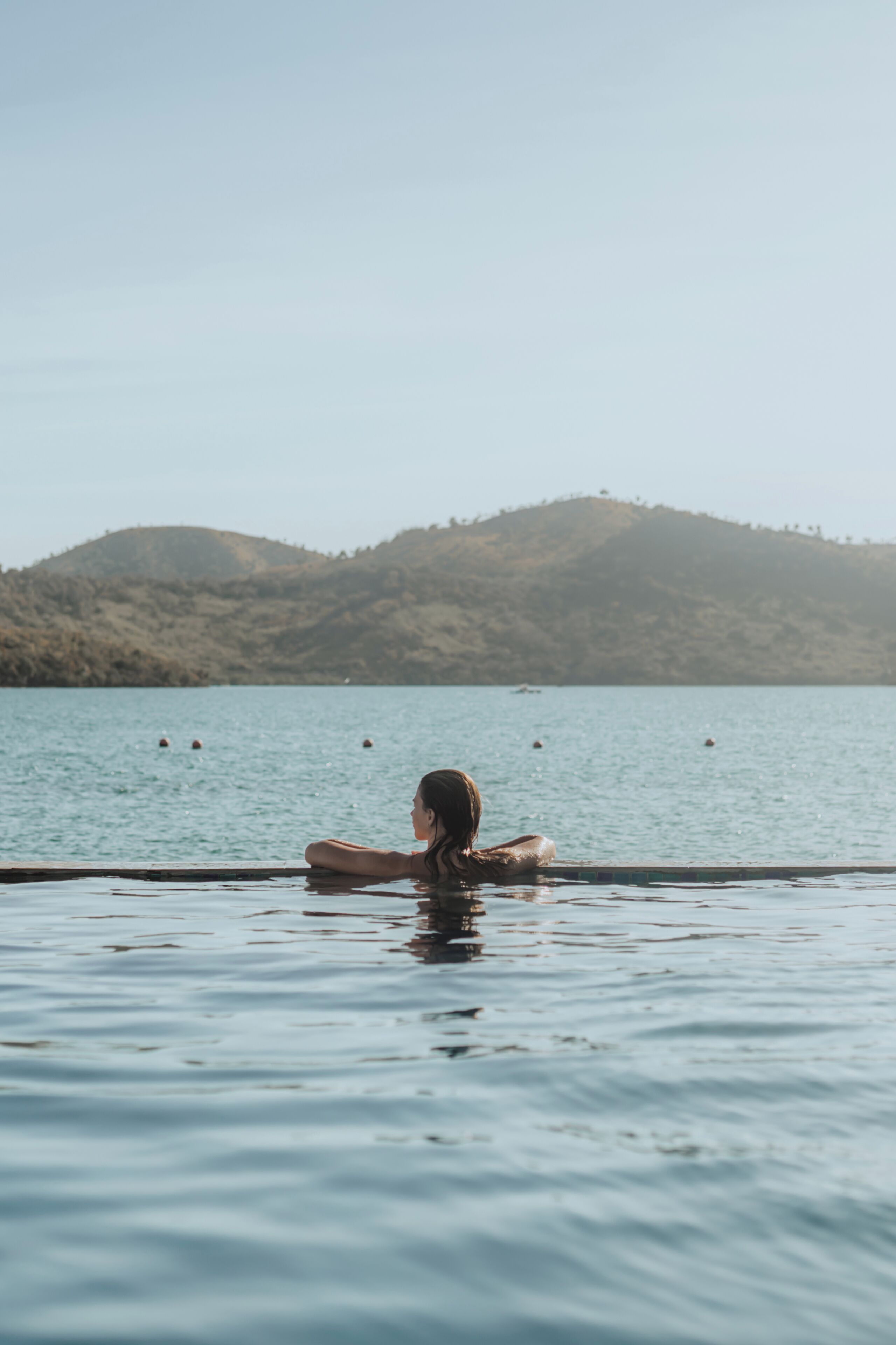 Una persona relajándose en una piscina con vistas a un paisaje montañoso y agua tranquila.