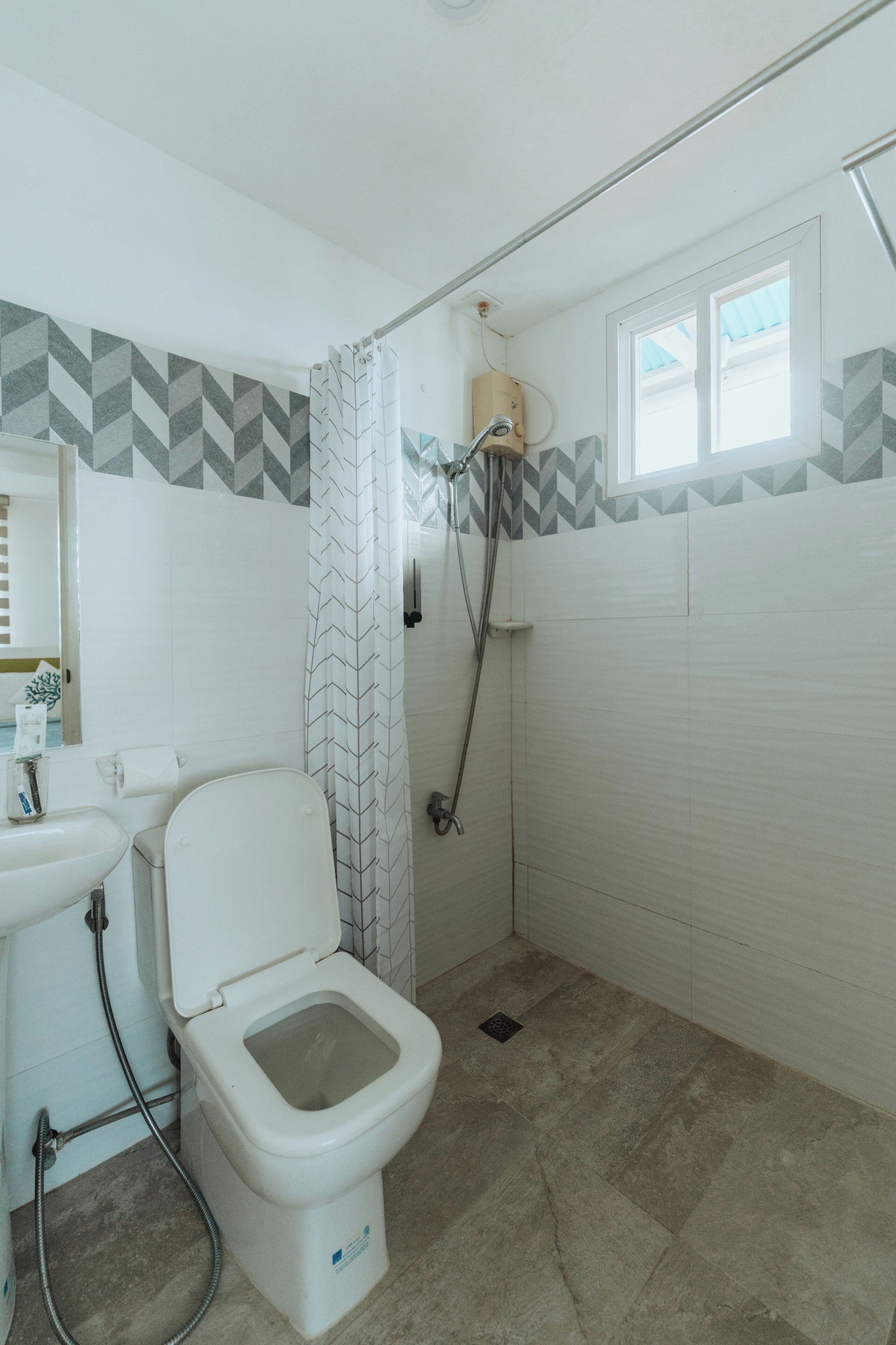 A bathroom with a toilet, sink, shower, and a window.