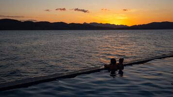 Ein Sonnenuntergang über ruhigem Wasser, im Vordergrund eine Silhouette einer Person und eines Hundes auf einem Steg.