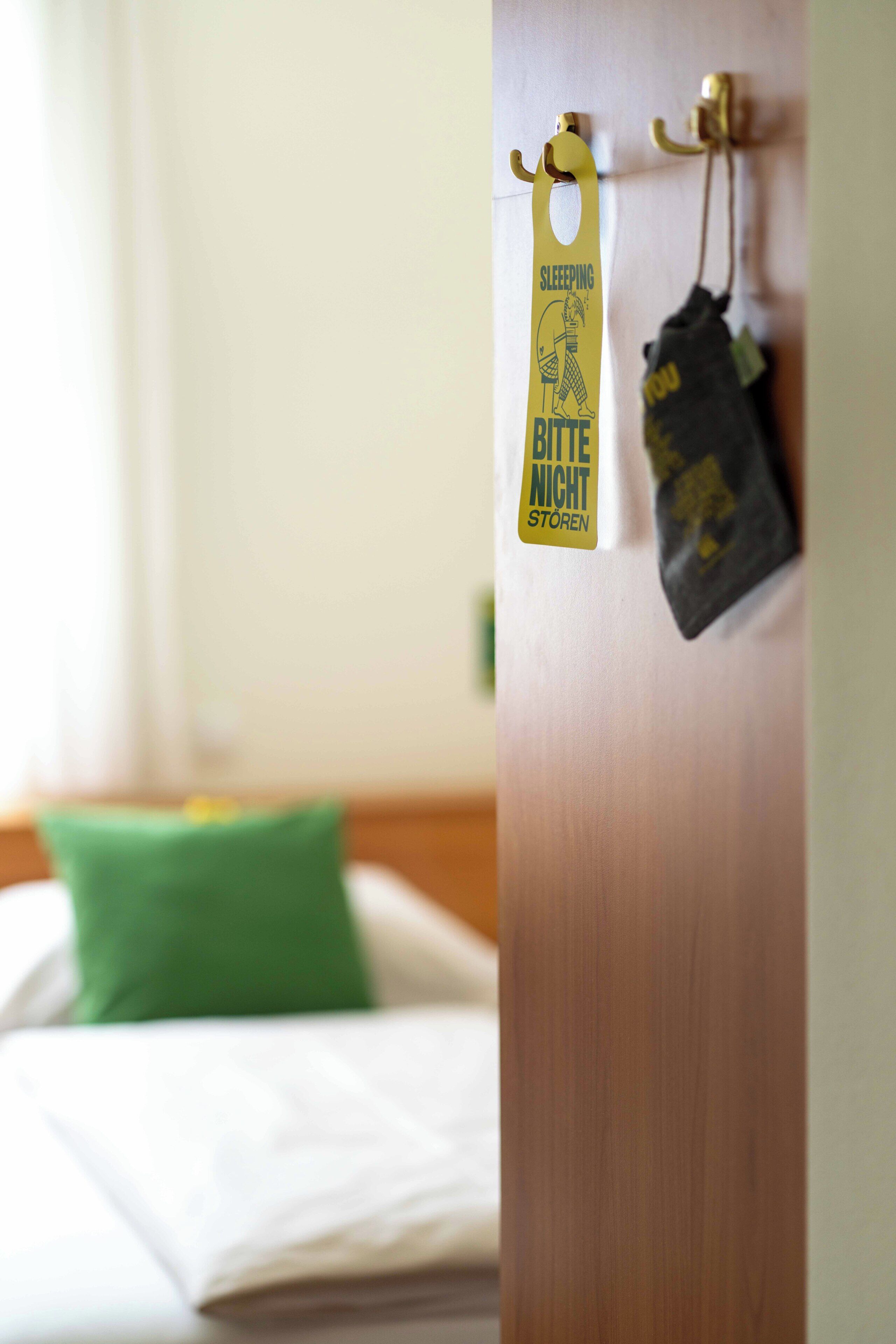 A hotel room with a bed, a green pillow, and a door with a yellow sign.