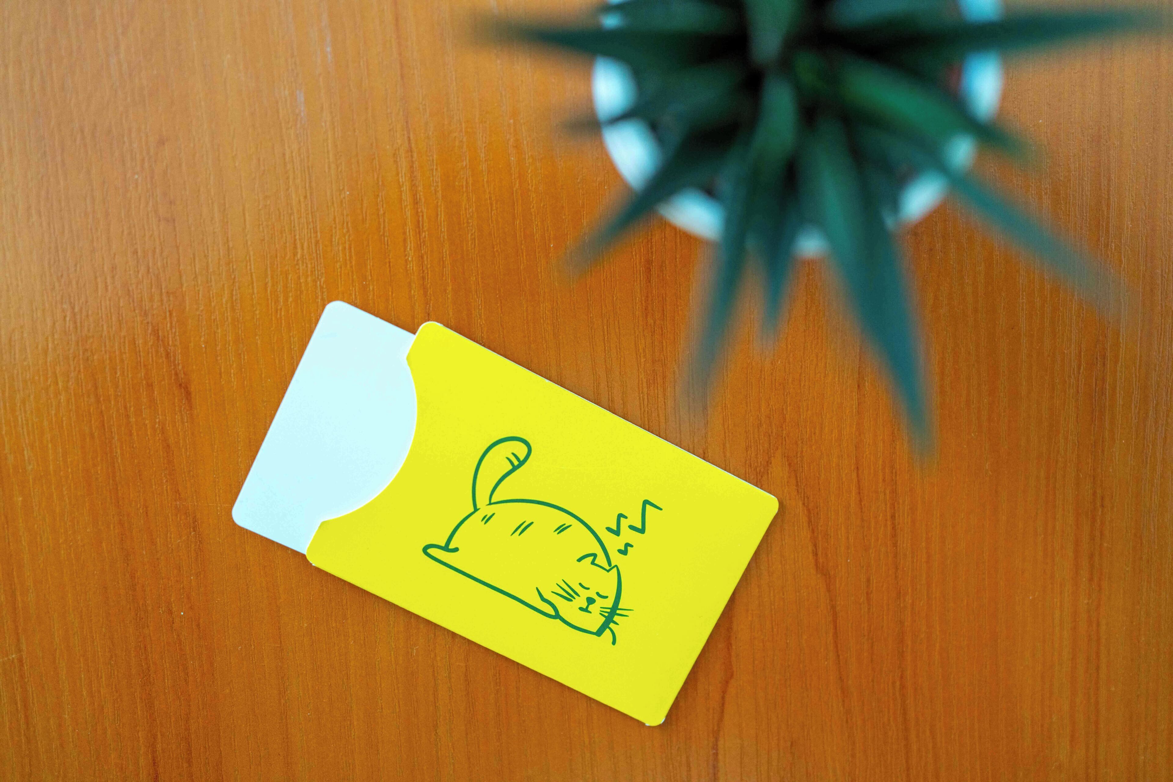 A yellow sticky note with a cat drawing on a wooden surface.
