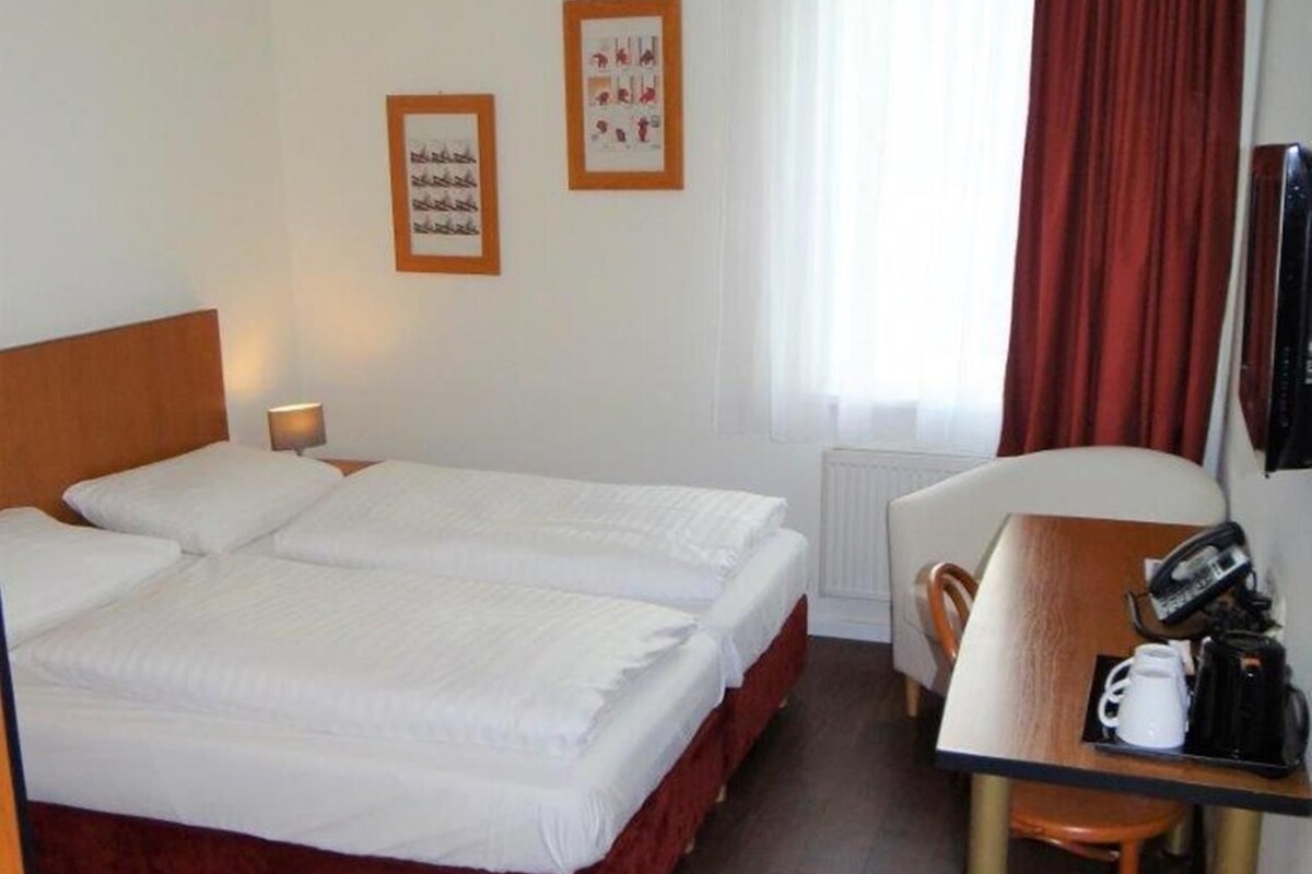 Habitación de hotel con cama doble, escritorio, teléfono y cafetera, además de una silla.