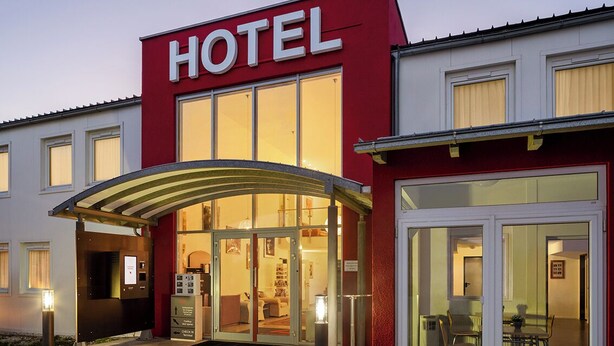 A hotel with a prominent 'HOTEL' sign, a covered entrance, and a visible interior with a reception area. - SLEEEP Hotel Sattledt (Sattledt)