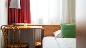 A hotel room with a bed, a desk with a lamp, a chair, and a window with curtains. - SLEEEP Hotel Sattledt (Sattledt)