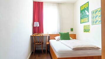 A small, neatly arranged bedroom with a bed, a desk, and a chair, a window with curtains, and wall decorations.
