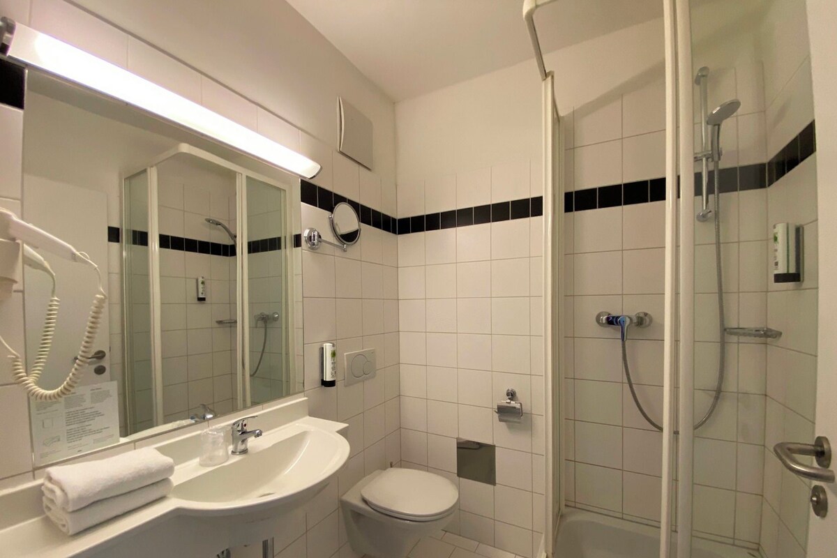 Uma casa de banho moderna com chuveiro em cabine de vidro, lavatório branco e sanita.
