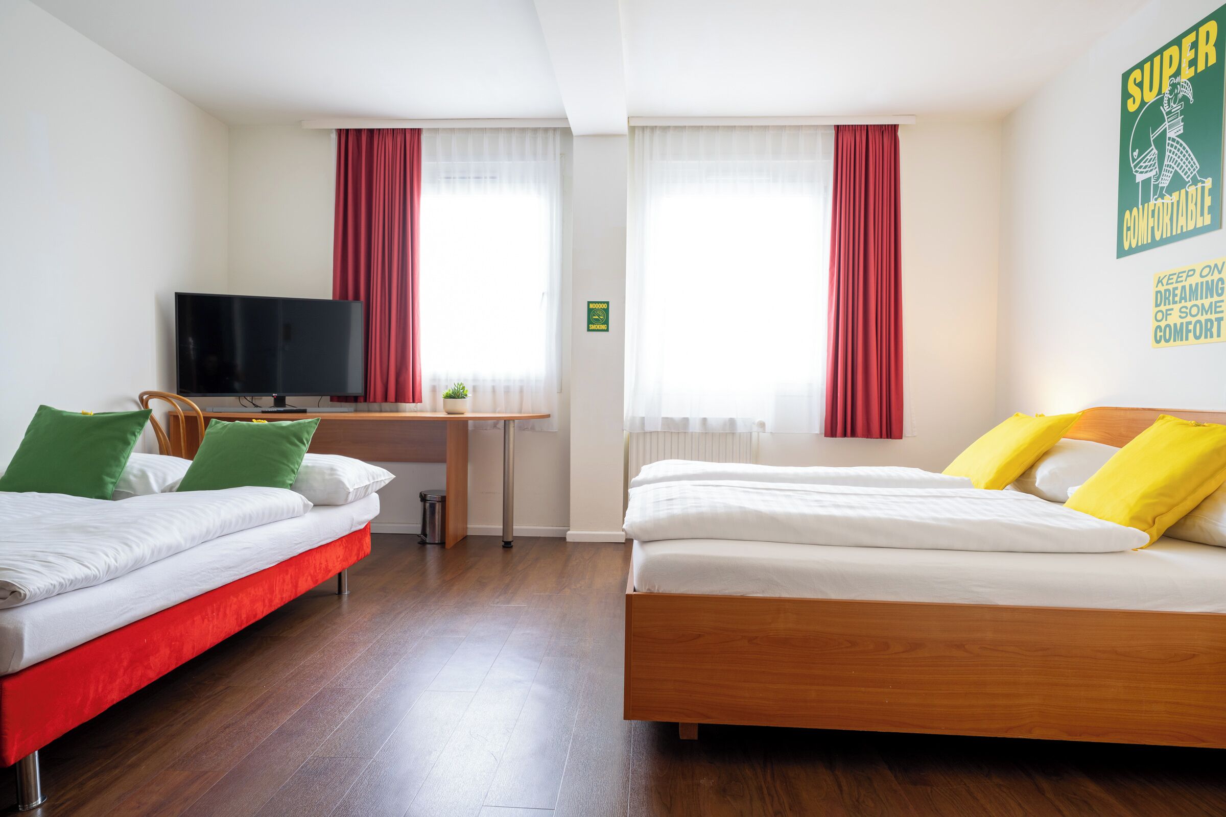 Ein Hotelzimmer mit zwei Betten, einem Schreibtisch, einem Fernseher und einem Fenster mit Vorhängen.