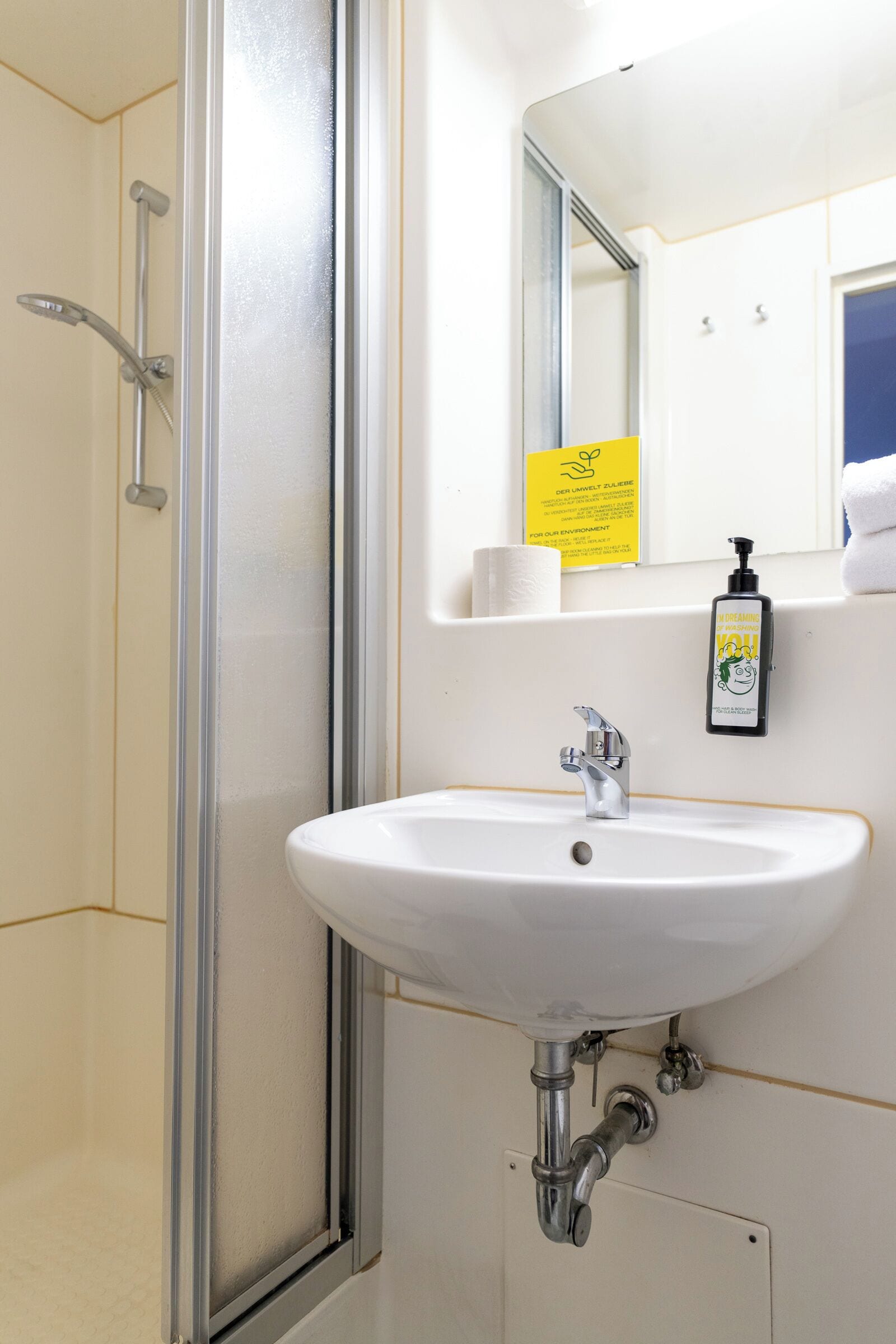 A bathroom with a white sink, a mirror, a shower, and a yellow sign.