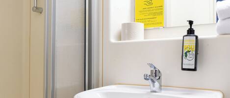 A bathroom with a white sink, a mirror, a shower, and a yellow sign.