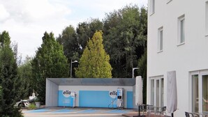 Un bâtiment arborant le logo « ella », une zone de stationnement et un arbre en arrière-plan.