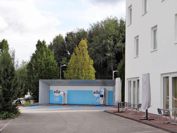 A building with 'ella' branding, a parking area, and a tree in the background. - SLEEEP Hotel Sattledt (Sattledt)