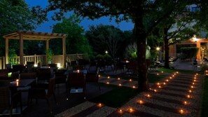 An outdoor dining area with tables and chairs, a pergola, and a pathway lined with candles. - Hotel Aretxarte (Zamudio)