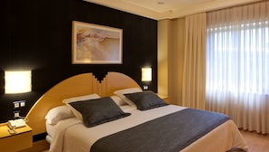 Ein Hotelzimmer mit einem großen Bett, zwei Nachttischen, einem Wandbild und einem Fenster mit Vorhängen.