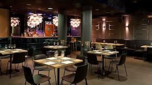 Ein Restaurant mit runden Tischen und Stühlen, einer Bar und hängenden Pendelleuchten.