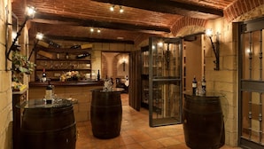 Ein rustikaler Innenraum mit freiliegenden Ziegeldecken, Holzbalken und einer Bar mit Weinflaschen und Gläsern.