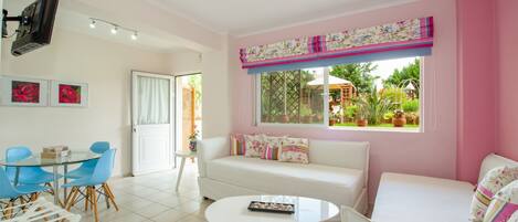 A bright living room with a white sofa, blue chairs, a round table, and a large window with a view of greenery.