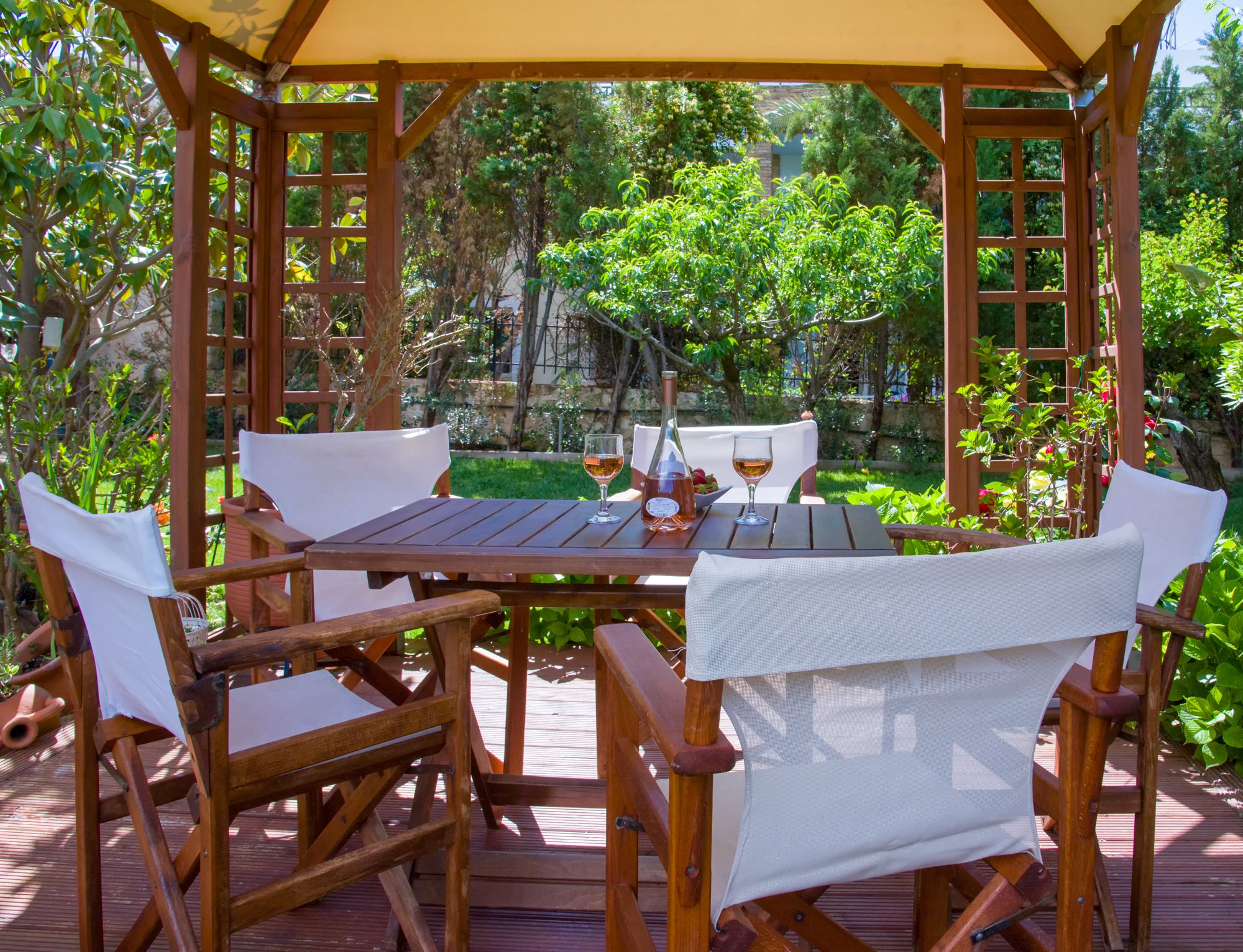A wooden pergola with a table and chairs, surrounded by lush greenery.