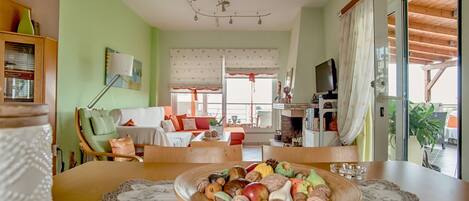 A cozy living room with a dining table set with fruits and nuts, a fireplace, and a television.