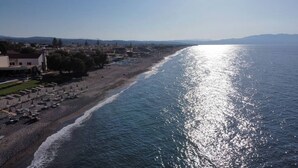 Una playa costera con sombrillas y tumbonas, cielo despejado y un mar tranquilo que refleja la luz del sol.