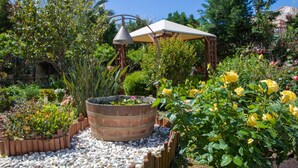 Un jardín con una jardinera de madera, rosas amarillas y una pérgola.
