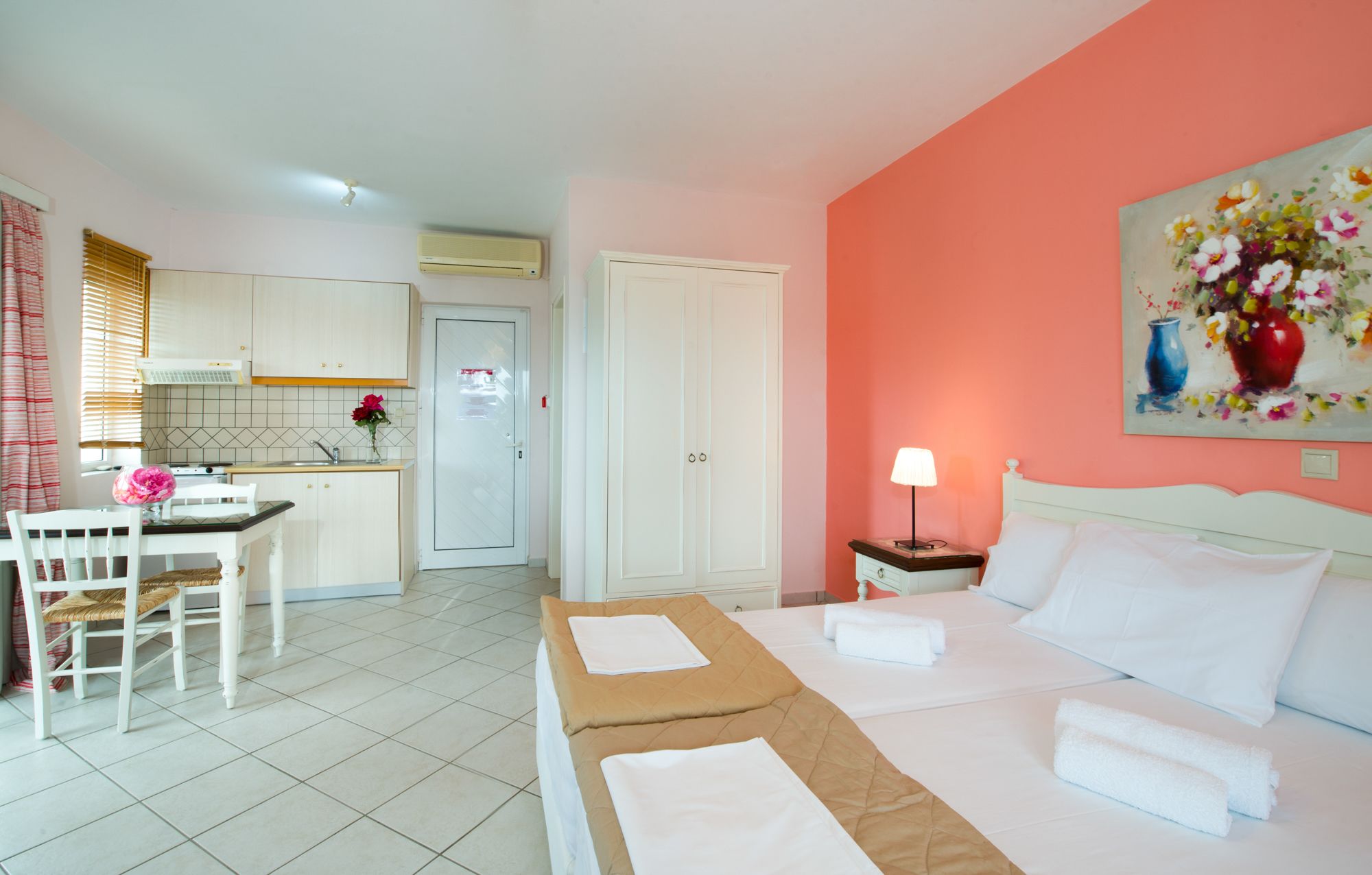 Een hotelkamer met een bed, nachtkastje, schilderij, bureau met stoel, en een kitchenette.