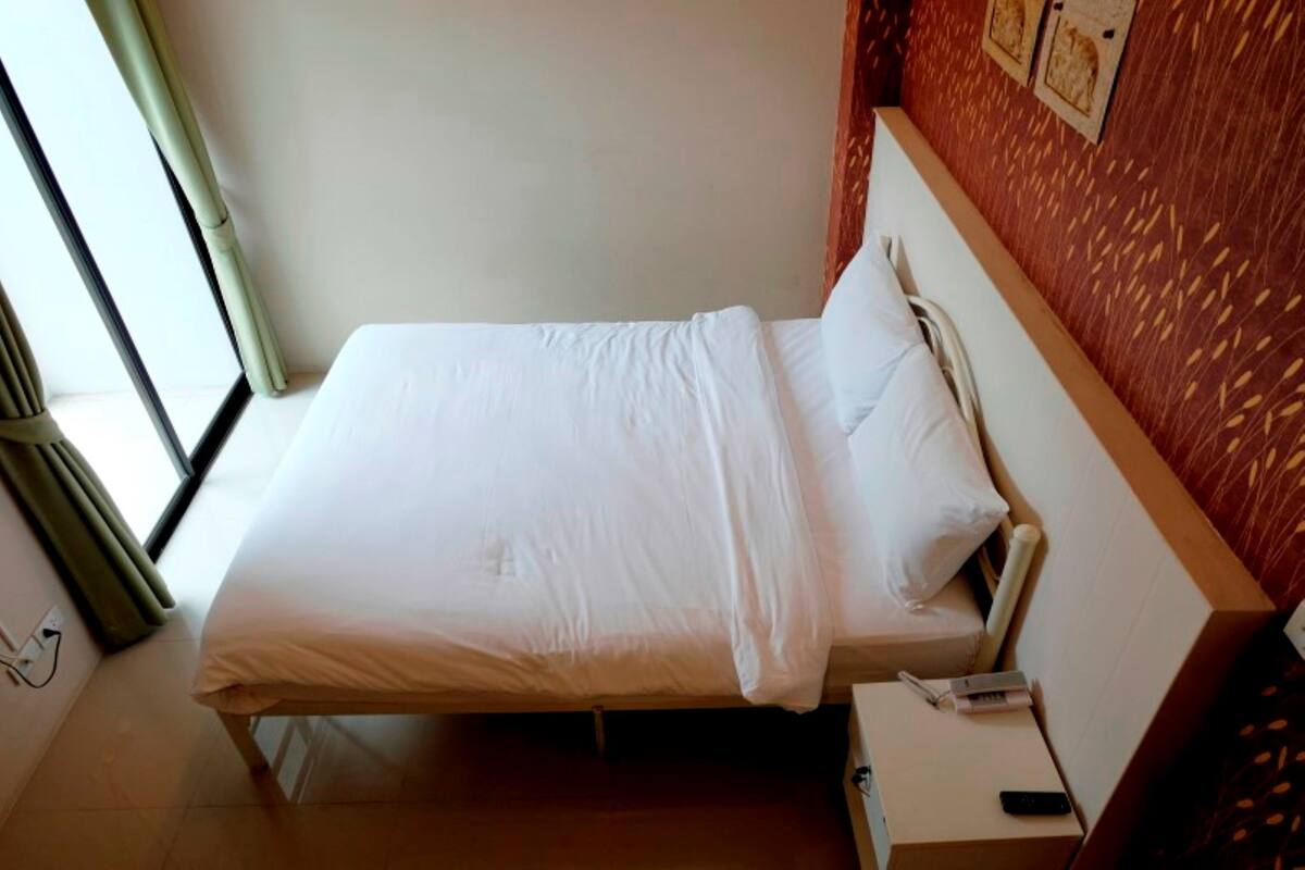 Quarto de hotel com uma cama, uma mesa de cabeceira e um controle remoto, e uma janela com cortinas.