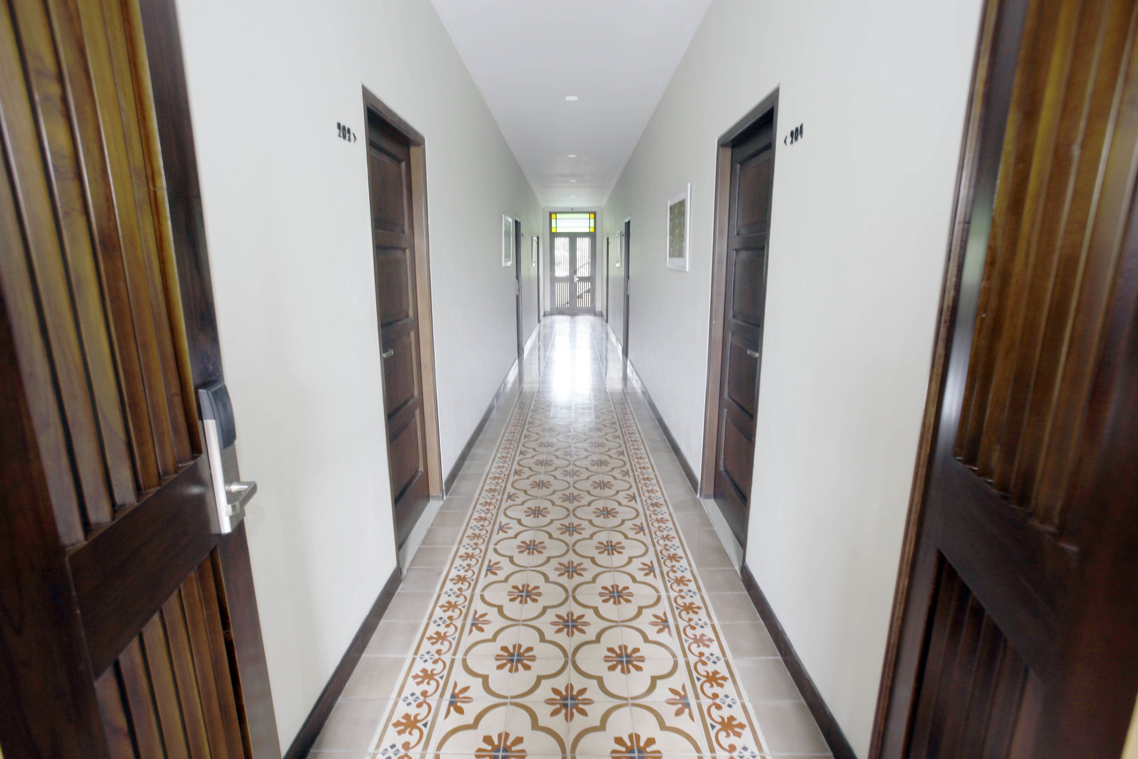 A hallway with patterned floor tiles, wooden doors, and a ceiling with recessed lighting.