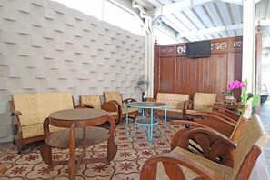 A covered outdoor seating area with wooden furniture and a patterned floor. - Rumah Kandjani (Depok)