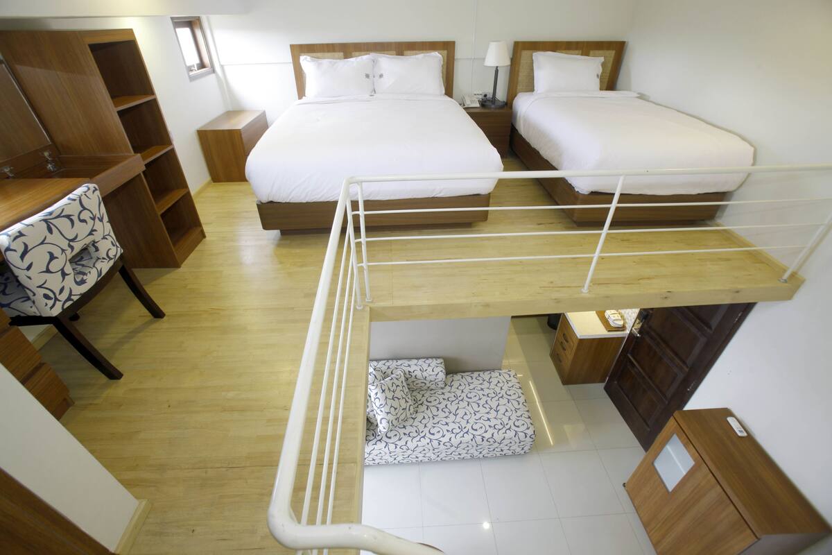 A hotel room with two beds, a desk, a chair, and a bunk bed.