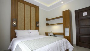 Cama bem arrumada com edredom branco e travesseiros, cabeceira de madeira com painel trançado, mesa de cabeceira com abajur e guarda-roupa de madeira.