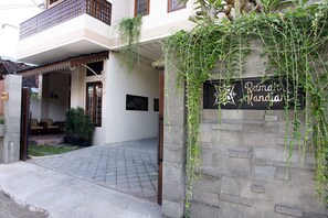 A two-story building with a balcony, a stone wall with a sign, and a paved entrance area. - Rumah Kandjani (Depok)