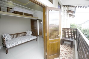 A balcony with a wooden bench, a sofa with patterned cushions, and a door leading to an interior space. - Rumah Kandjani (Depok)