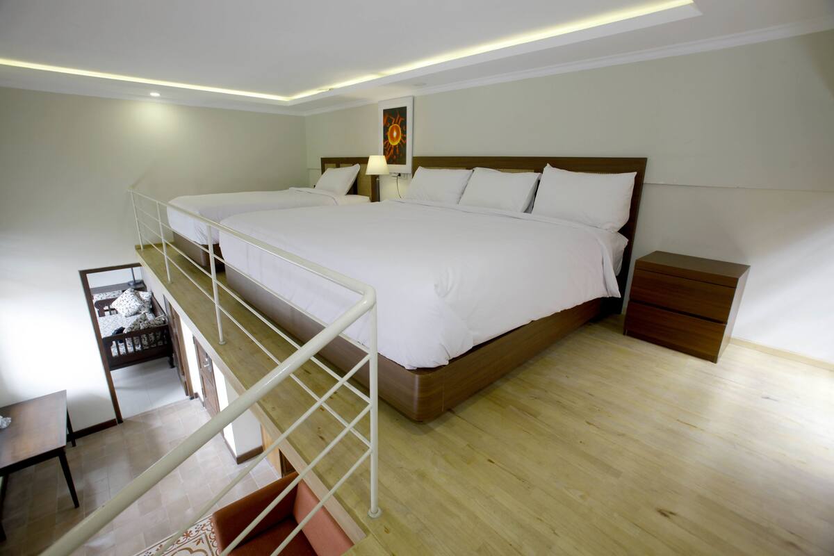 A bedroom with a large bed, a nightstand, a desk, and a staircase.