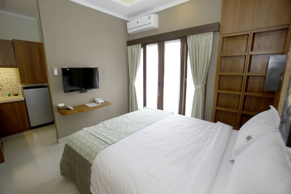 A hotel room with a bed, a TV, a small kitchenette, and a window with curtains. - Rumah Kandjani (Depok)