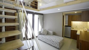 Um apartamento moderno e compacto, com um quarto no mezanino, uma kitchenette e uma escada.
